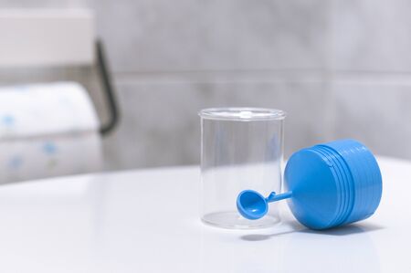 A stool sample container for fecal tests in the bathroom with a roll of toilet paper on the background.の写真素材