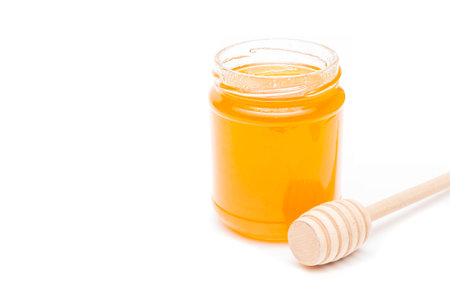 Jar full of honey and honey dipper on a white backgroundの写真素材