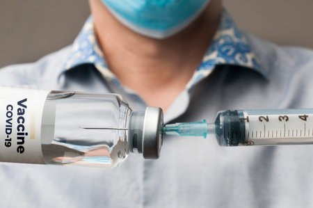 Doctor with surgical mask fills a syringe with the covid-19 vaccine to inject it