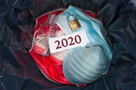 Goodbye 2020 concept: The inside of a trashbin with surgical masks, sanitizing gel, a padlock and a...