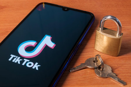 Carrara, Italy - January 22, 2021 - Smartphone showing the tiktok logo on a wooden table with a lock...