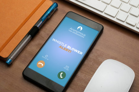 Whistleblowing concept: smartphone next to an orange notepad on wooden table show a whistle blower...