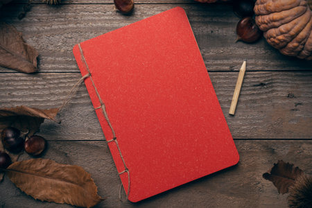 Autumn concept: red notebook on a wooden floor sorrounded by chestnuts, pumpkins and dry leaves
