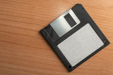Old 3.5 black floppy disk with blank label on a wooden tableの写真素材