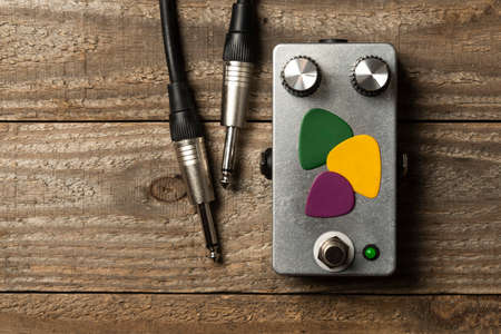 Metal blank guitar pedal with some picks and a cable on wooden floorの写真素材