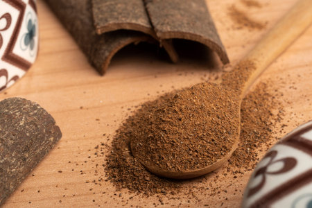 Wooden spoon filled with ground cinnamon on the table with some cinnamon sticks