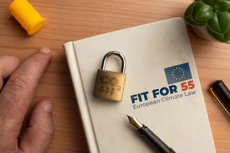 Fit for 55 european climate law concept: a book on a wooden table with a man hand a lock and a penの写真素材