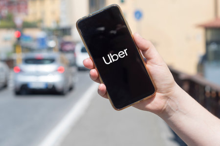 Carrara, Italy - July 13, 2022 - Woman holds a smartphone on a background of cars showing the Uber logoのeditorial素材