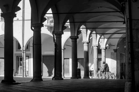 Person with anti Covid mask pushes a bicycle under a colonnade in an empty square due to the lockdownの写真素材