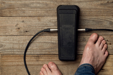 Barefoot guitar player uses a wah wah pedal on a wooden floorの写真素材