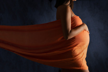 Pregnant woman wrapped in a orange drape on blue backgroundの写真素材