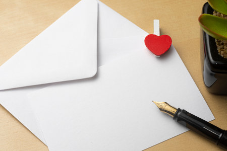 Valentine's day concept: envelope with blank ticket decorated with a heart and a fountain pen placed on topの写真素材