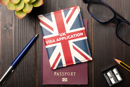 UK visa application concept: a union jack colored wallet over a generic passport on a wooden desktop