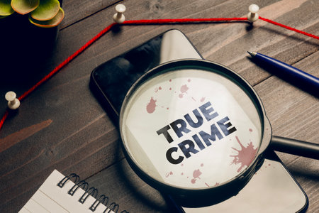True crime concept: a magnifying glass above a smartphone on a detective's deskの写真素材