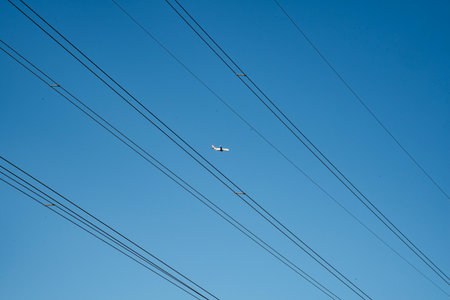 Airplane flying in the blue sky with wires in the foreground.の写真素材