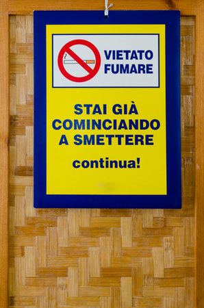 "Vietato Fumare" ("No Smoking") signboard in italian language with the message "Se stai cominciando a smettere continua" ("if you're trying to stop go on"), hanging from a wooden screenの写真素材