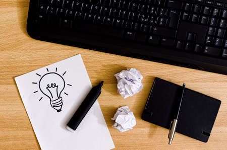 computer keyboard on a desk with agenda, marker pen, crumpled sheets and a white sheet with a a light bulb drawingの写真素材