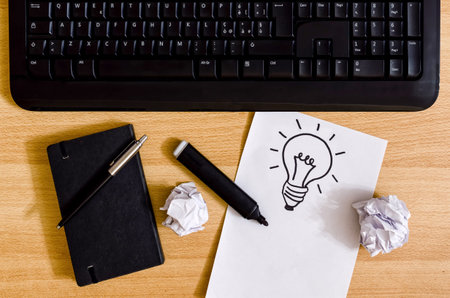 computer keyboard on a desk with agenda, marker pen, crumpled sheets and a white sheet with a a light bulb drawingの写真素材