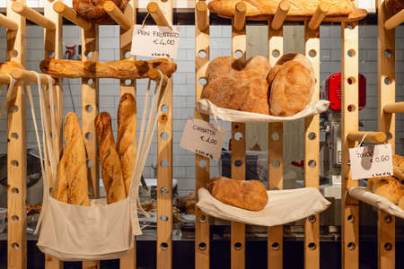 Inside view of an italian bakery shop with the kitchen in background and different bread types: pan fruttato (fruity bread), ciabatta (ciabatta bread) and tondo (round shaped bread).の写真素材