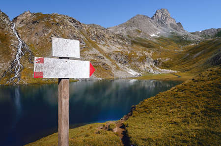 The Lac Bleu in Chianale, mountain lake in the italian alps of Cuneo, Piedmont, with white blank sign for trekkers pointing at the nearby peakの写真素材