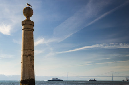 old stone column in the harbor of Praca do Comercio, Lisbon main square, with a seagull looking to...