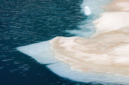 Detail of snow and ice slowly melting on the surface of a mountain lake with strong contrast between the blue of the water and the white of the icebergの写真素材