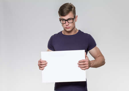 Handsome young man holding a white board in a studio with grey background.の写真素材