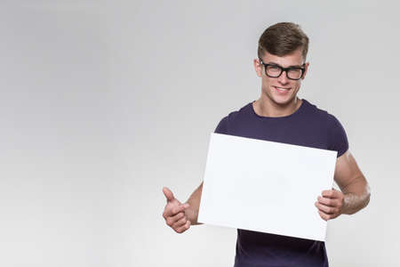 Handsome young man holding a white board in a studio with grey background.の写真素材