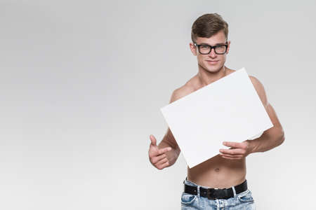 Shirtless handsome young man holding a white board in a studio with grey background.の写真素材