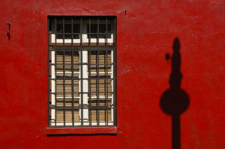 latticed window on a red wall with a pole shadowの写真素材