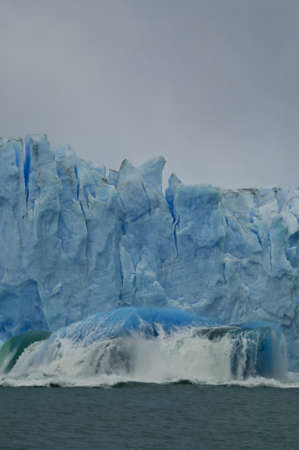 blue iceberg falls out of massive glacierの写真素材