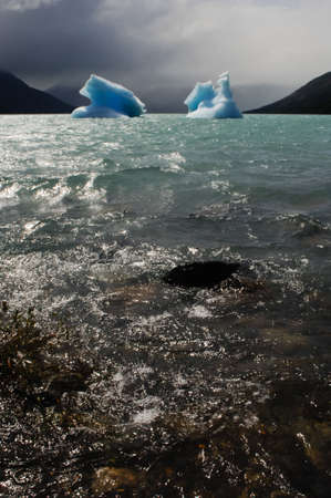two icebergs floating on the sea with mountains in the backgroundの写真素材