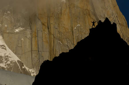 rockclimber on cliffs facing the massive red granite wall of fitz roy peak, los glaciares national park, patagonia, argentinaの写真素材