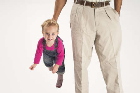 concept of caring, father holding happy baby toddler girl suspended by suspendersの写真素材