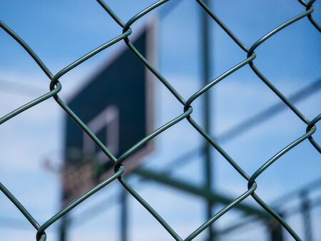 Wired fence pattern with a basketball hoop as a background. Steel wire mesh and a blue sky.の写真素材