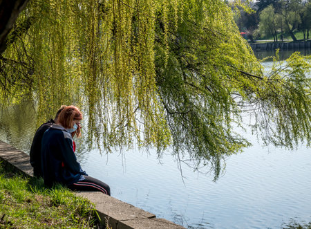 Bucharest/Romania - 03.19.2020: Women in the park wearing wearing a face mask for protection against Coronavirus pandemic. Girl at the edge of a lake.のeditorial素材