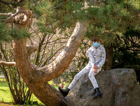 Bucharest/Romania - 03.19.2020: Small girl in the park wearing a face mask for protection against Coronavirus pandemic. Girl sitting on a rock in the park.のeditorial素材