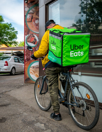 Bucharest/Romania - 05.01.2020: Uber Eats courier on a bicycle waiting to take the order in front of a pastry shop.のeditorial素材