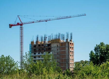Construction crane and unfinished apartment or office building against blue sky. Construction site of a buildingの写真素材
