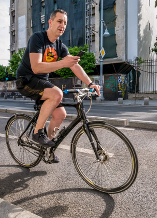 Bucharest/Romania - 05.16.2020: Man texting on his smartphone while riding a bicycle in the center of Bucharest. People enjoying a nice day in the center of Bucharest.のeditorial素材