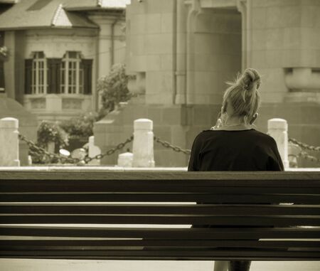 Young blonde girl sitting on a bench. Vintage look of a lonely girl on a bench.の写真素材
