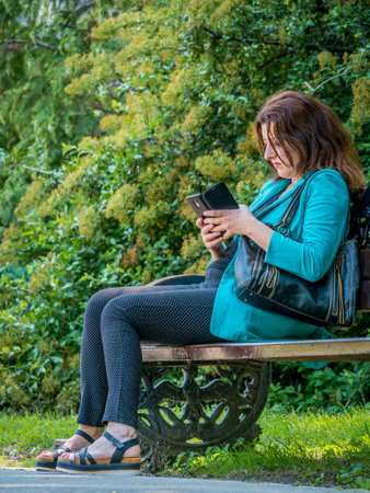 Bucharest/Romania - 05.30.2020: Woman sitting on a bench in the park and looking at her phone. Smart phone addiction conceptのeditorial素材