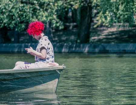 Bucharest/Romania - 05.30.2020: Girl with red hair in a boat looking at her phone. Smart phone addiction concept.のeditorial素材