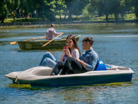 Bucharest/ Romania - 05.30.2020 Couple on a pedal boat in Cismigiu park. Girl looking at her smartphone while pedal boating. Smartphone addiction concept.のeditorial素材