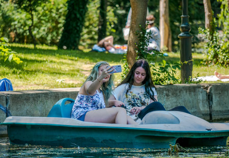 Bucharest/ Romania - 05.30.2020: Two girls on a pedal boat in Cismigiu park. Girl looking taking a selfie with her smartphone while pedal boating. Smartphone addiction concept.のeditorial素材