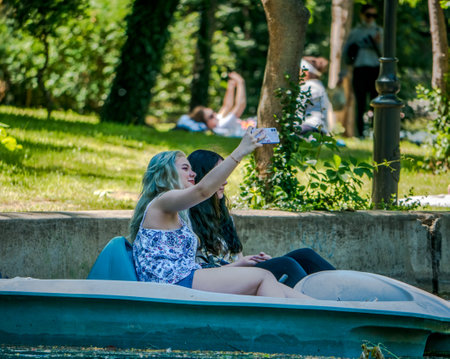Bucharest/ Romania - 05.30.2020: Two girls on a pedal boat in Cismigiu park. Girl looking taking a selfie with her smartphone while pedal boating. Smartphone addiction concept.のeditorial素材