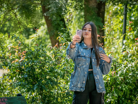 Bucharest/ Romania - 05.30.2020: Young girl taking a selfie with her smartphone. Girl in Cismigiu park, in Bucharest. Smartphone addiction concept.のeditorial素材