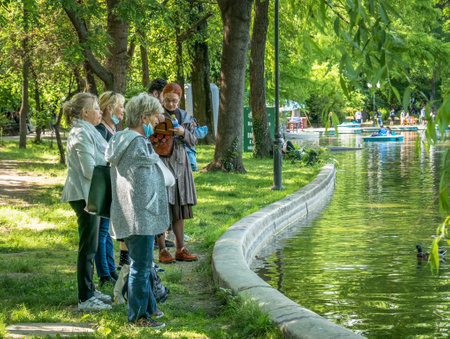 Bucharest/Romania - 05.30.2020: Group of seniors at the edge of a lake watching the ducks . Old women relaxing in the Cismigiu park.のeditorial素材