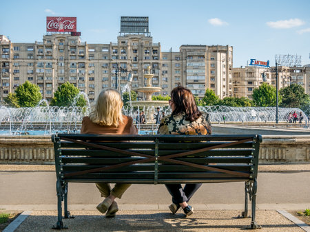 Bucharest/Romania - 05.30.2020: Two women on a bench lookink at the artesian water fountain in Unirii Square, Bucharest.のeditorial素材