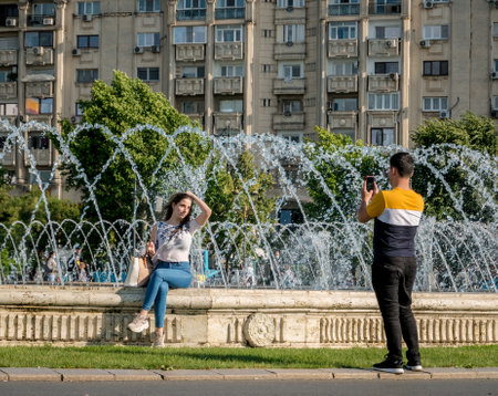 Bucharest/Romania - 05.30.2020: Young man taking a picture to his girlfriend with the water fountains in the backgroundのeditorial素材